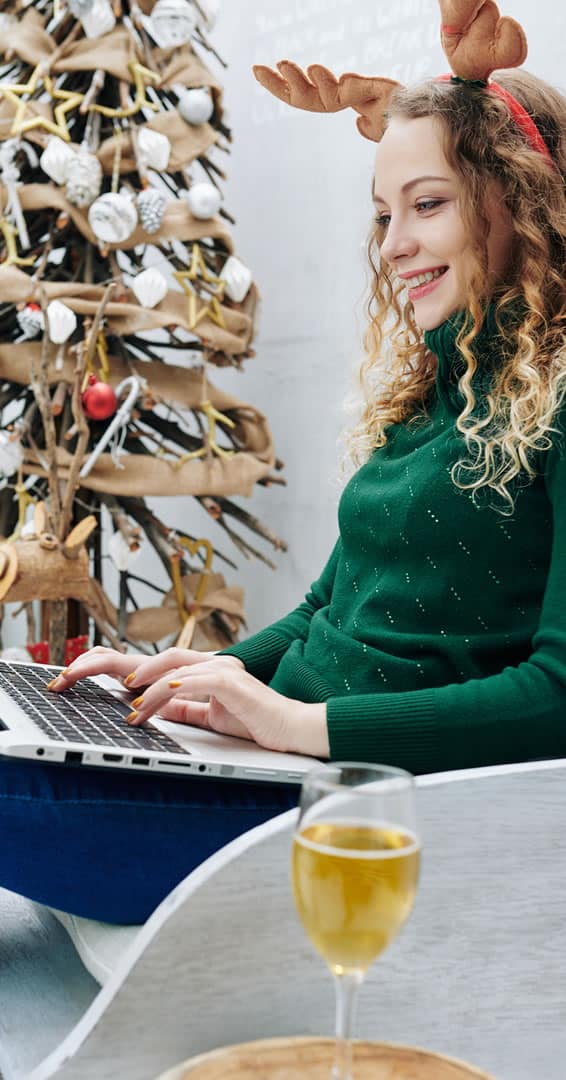 Woman with antlers using laptop near Christmas tree
