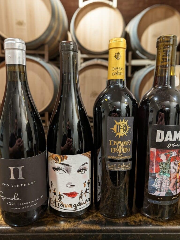 Four wine bottles displayed in front of barrels.